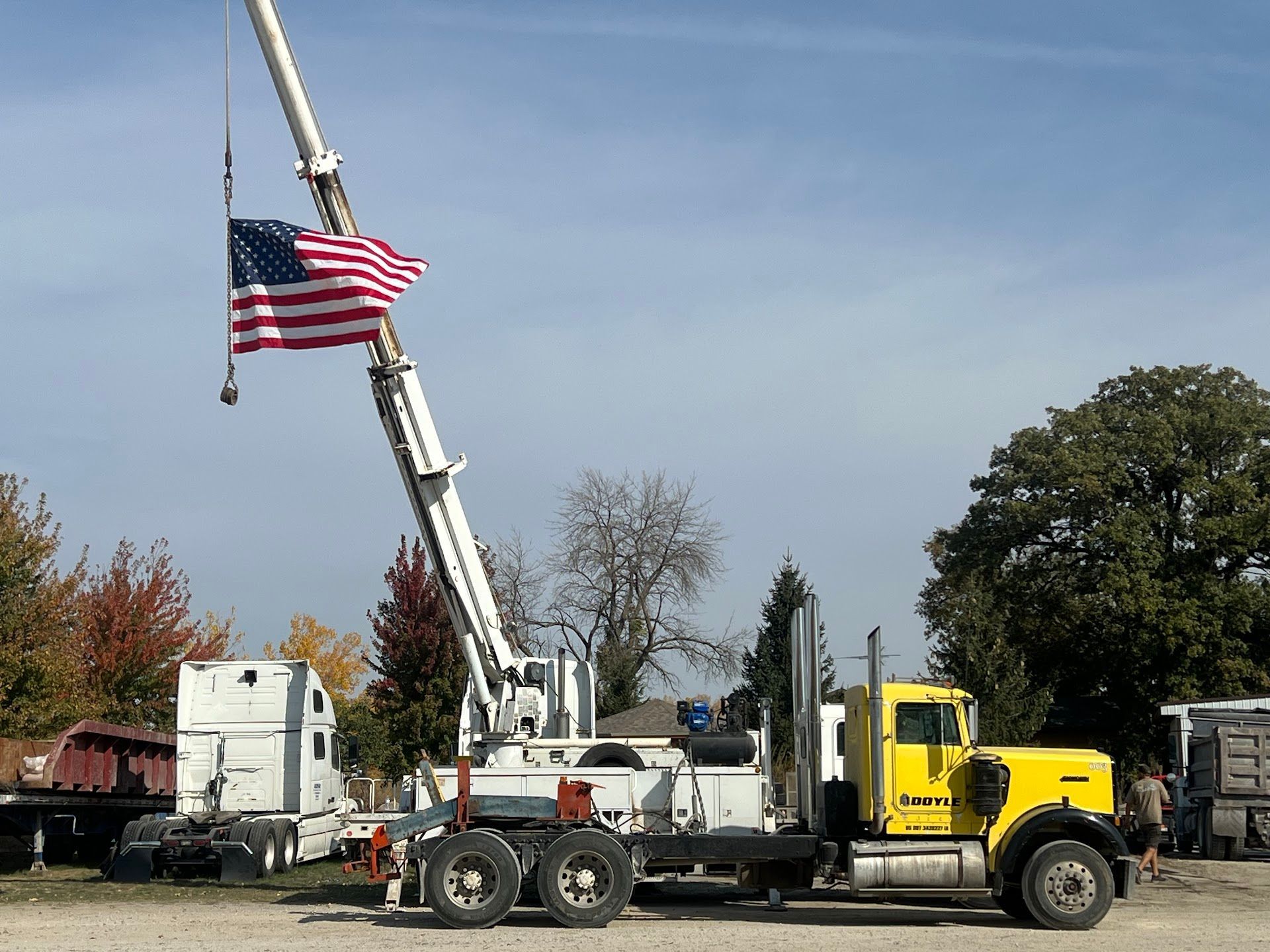 A yellow semi-truck with crane holding an American flag against a blue sky | Doyle Diesel