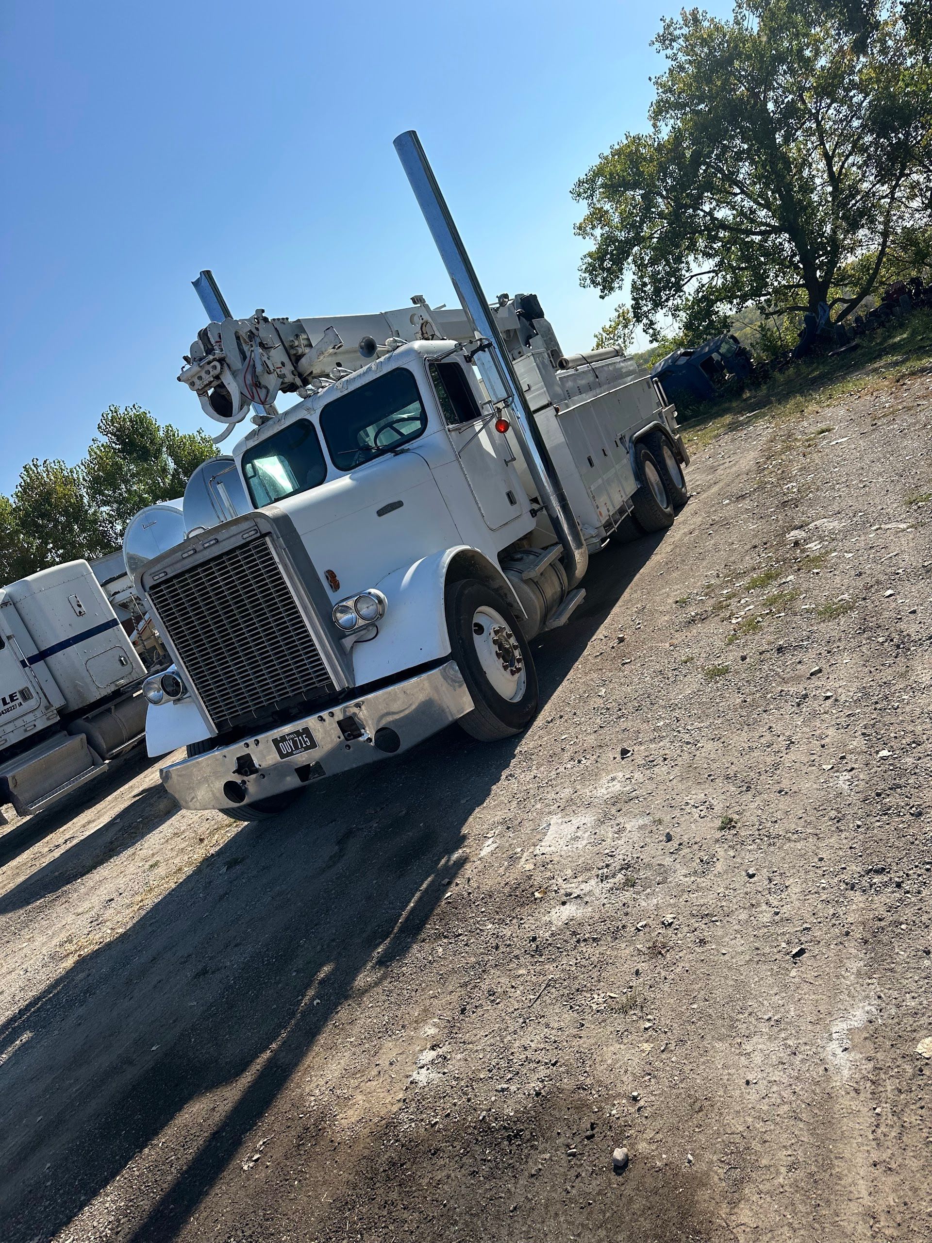 White tow truck on gravel road under a blue sky, near trees | Doyle Diesel