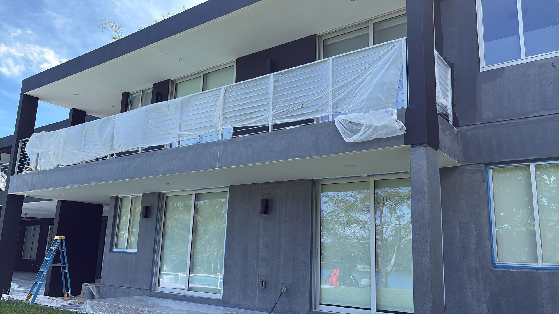 Exterior view of a two-story modern building with balcony covered in protective sheeting.
