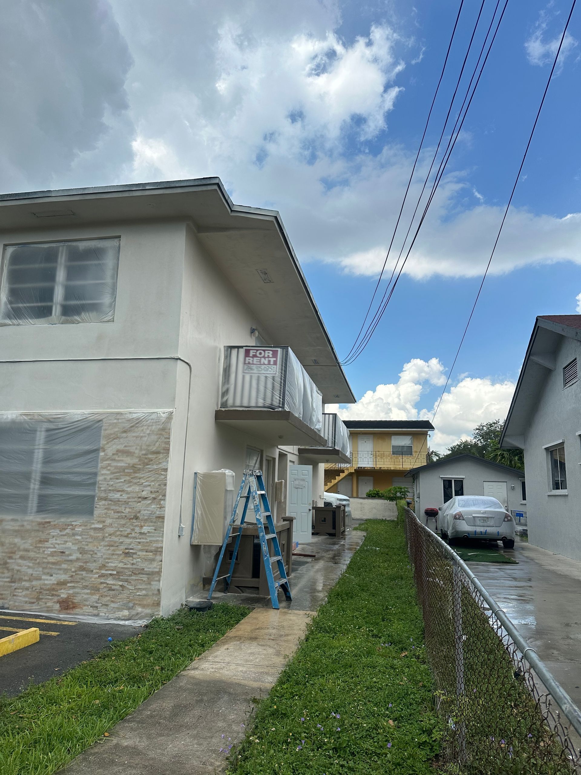 Two-story building exterior with stone and stucco facade, a balcony, and a blue ladder outside.