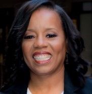 A woman is smiling for the camera while wearing a black jacket and white shirt.