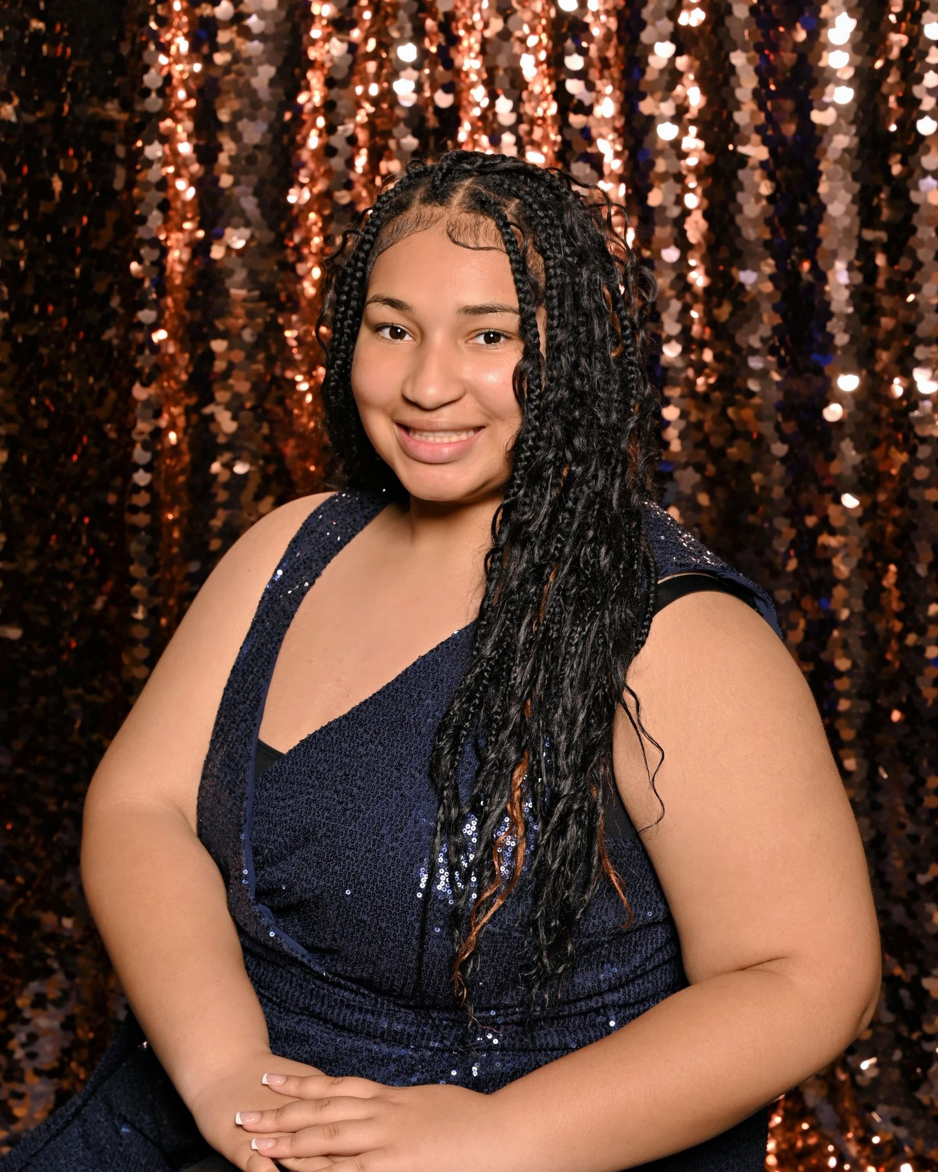 Woman with long, dark braids, in a sparkly blue dress, smiling in front of a gold backdrop.
