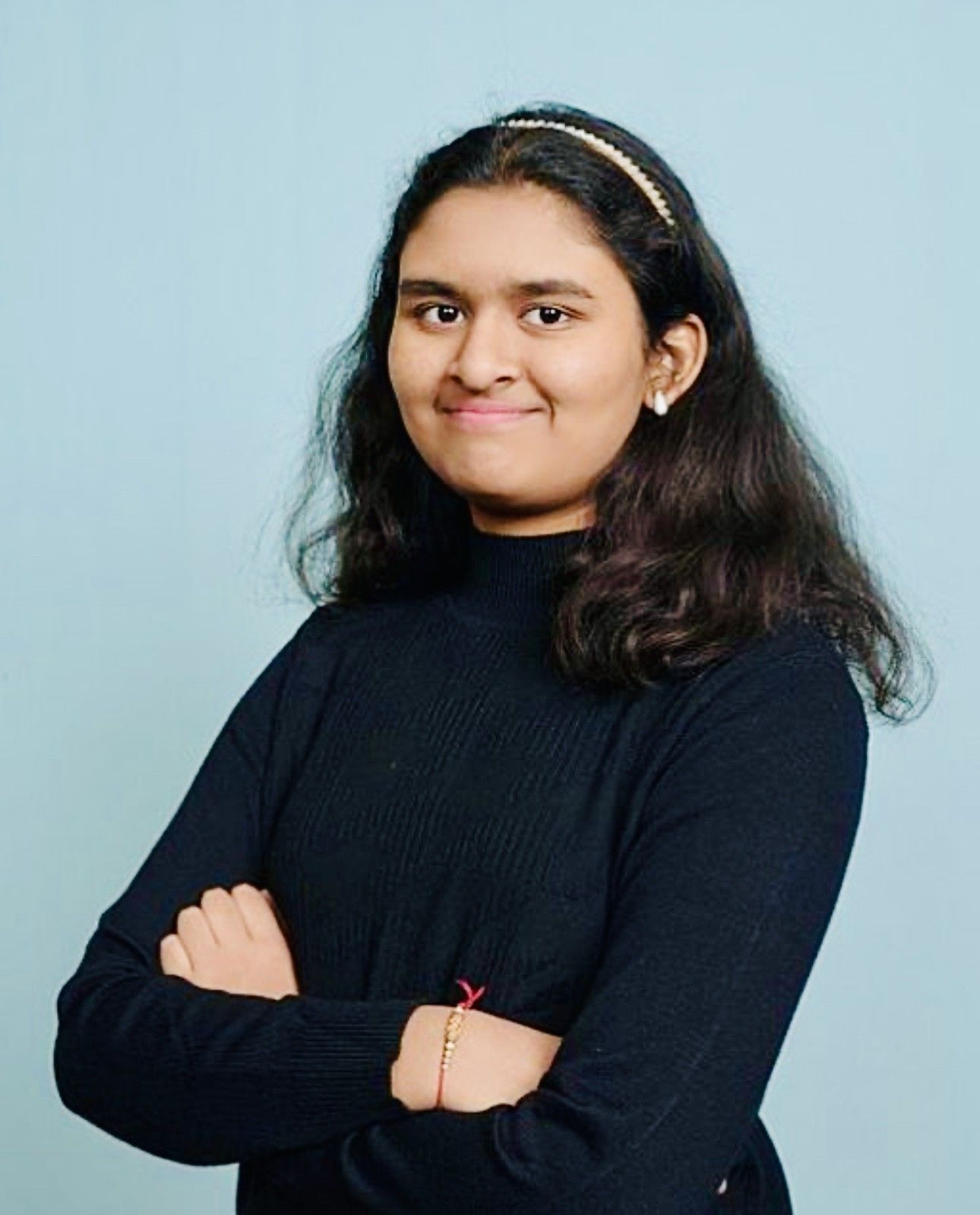 Woman with long, dark braids, in a sparkly blue dress, smiling in front of a gold backdrop.