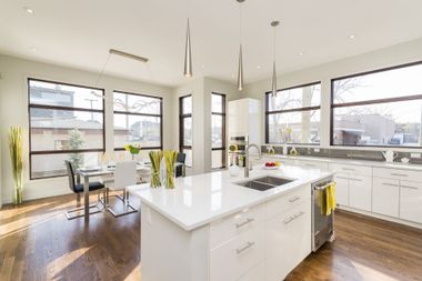 Bright, modern kitchen with white island, stainless steel appliances, and large windows. Dark wood floors.