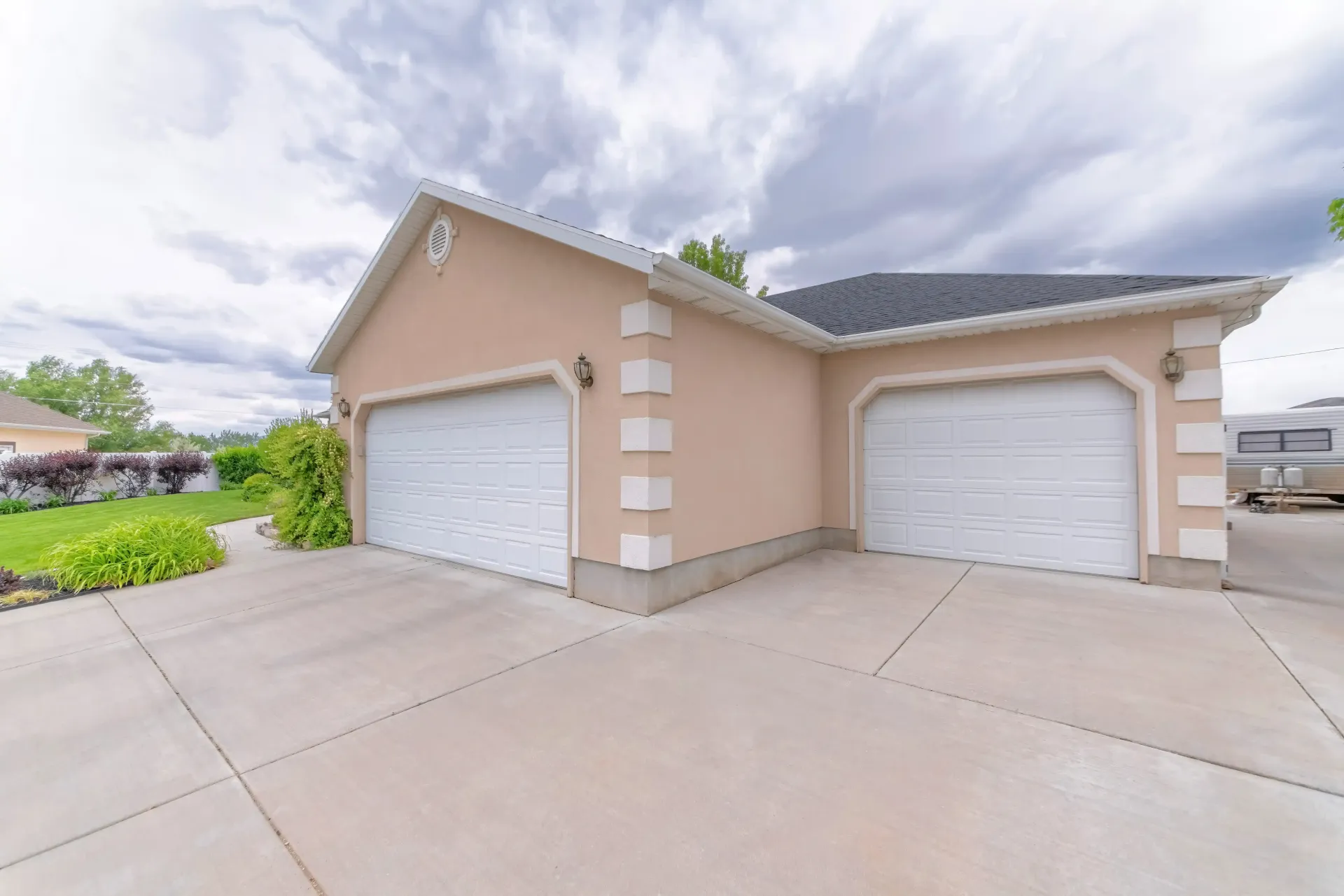 A concrete driveway and beige house with two white garage doors