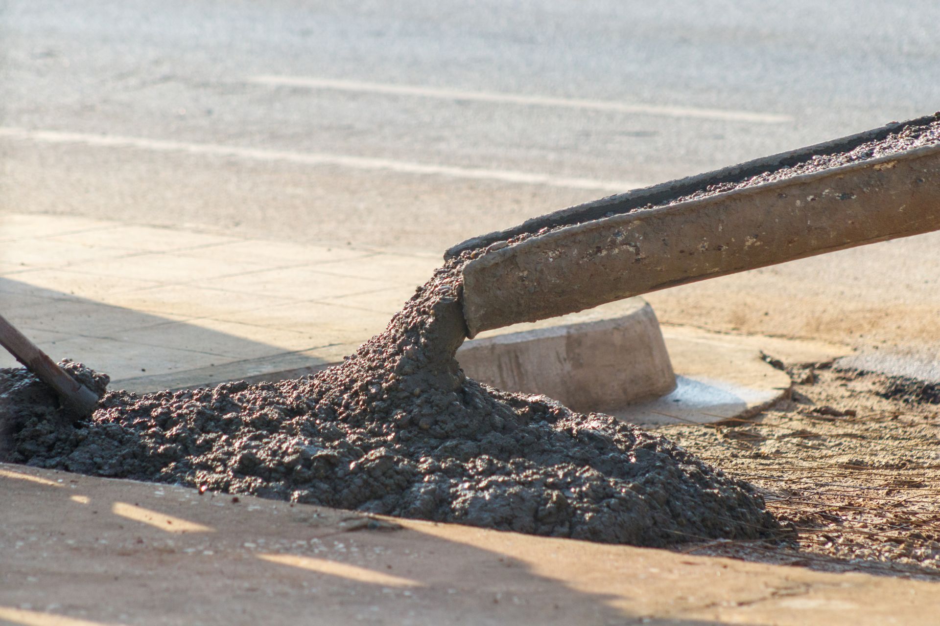 Concrete pouring from a chute onto a sidewalk.