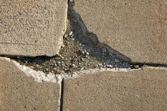 Close-up of cracked concrete paving stones, showing crumbling grout and visible aggregate.