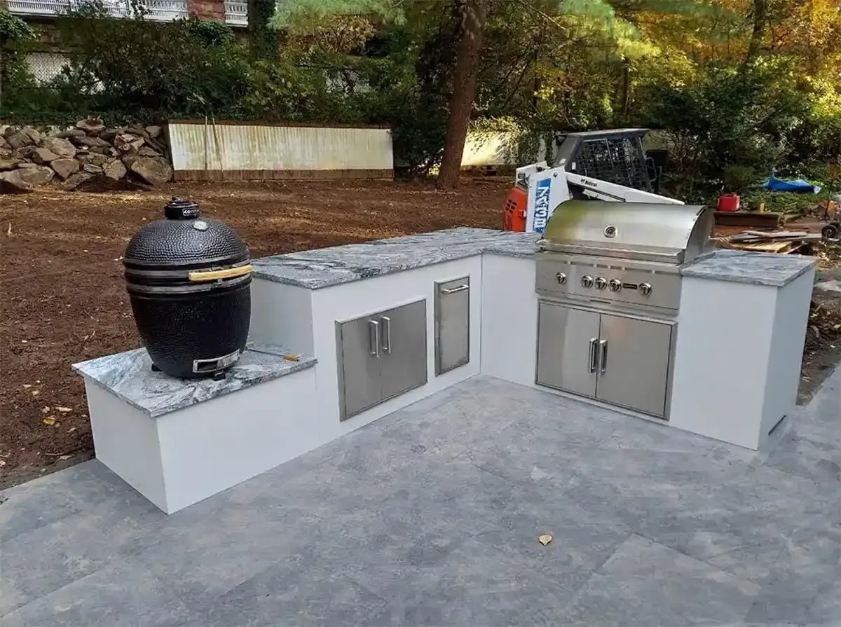 An L-shaped outdoor kitchen with a stone countertop, white stucco base, stainless steel cabinets, a grill, and a smoker.