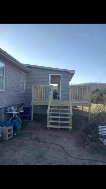 Wooden deck with stairs leading to a doorway, next to a house with blue siding.