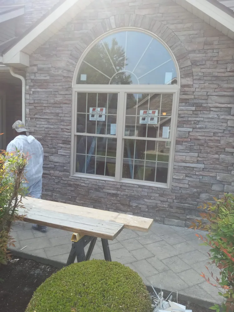 Person in protective suit near a window. Stone-covered building exterior with a wooden work table in front of the window.
