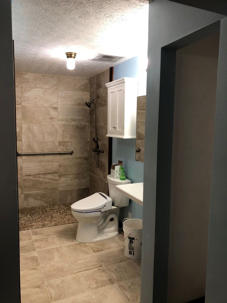 Bathroom with tiled shower, toilet, sink, and blue wall, viewed from doorway.