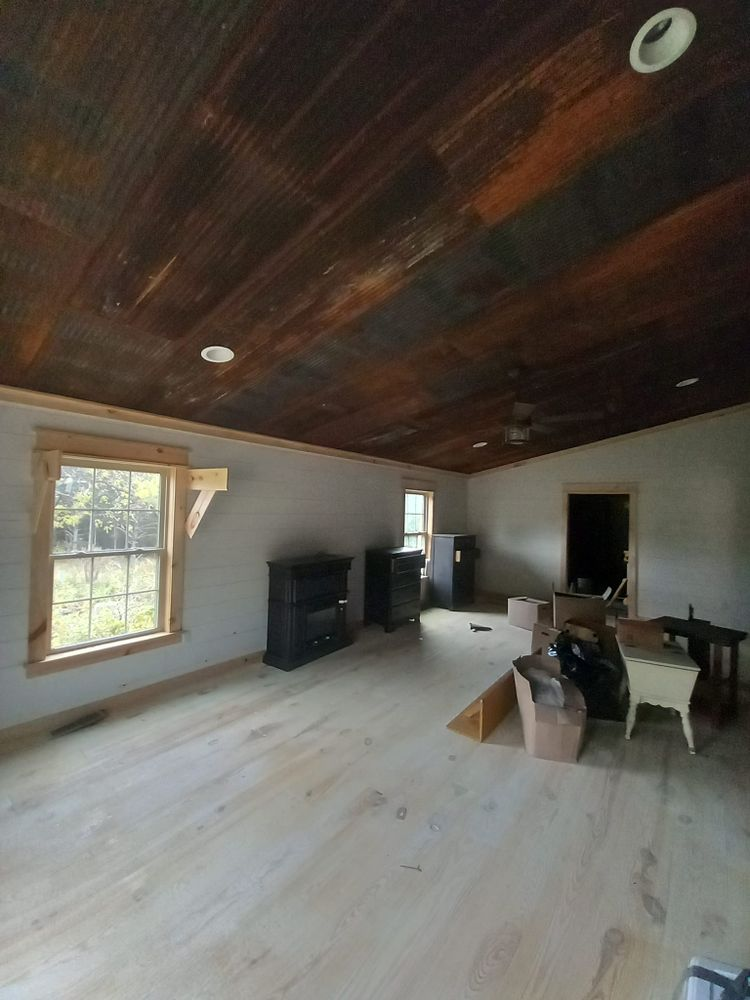 Open room with wood ceiling, white walls, wood floor, window, fireplace.