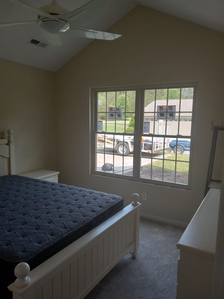 Bedroom with white bed, dresser, and window with a view of a truck.