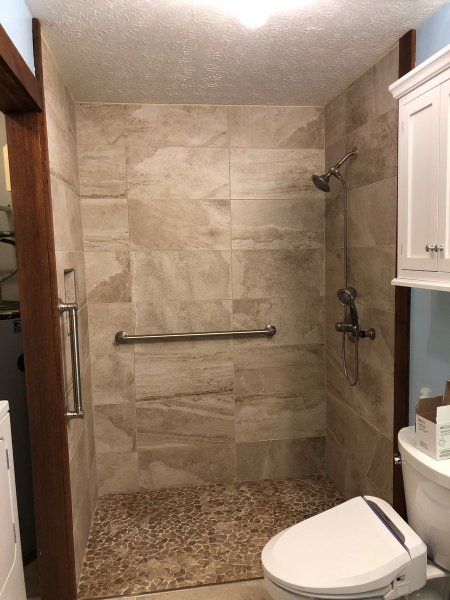 Bathroom with tile shower, pebble floor, grab bar, and a toilet.
