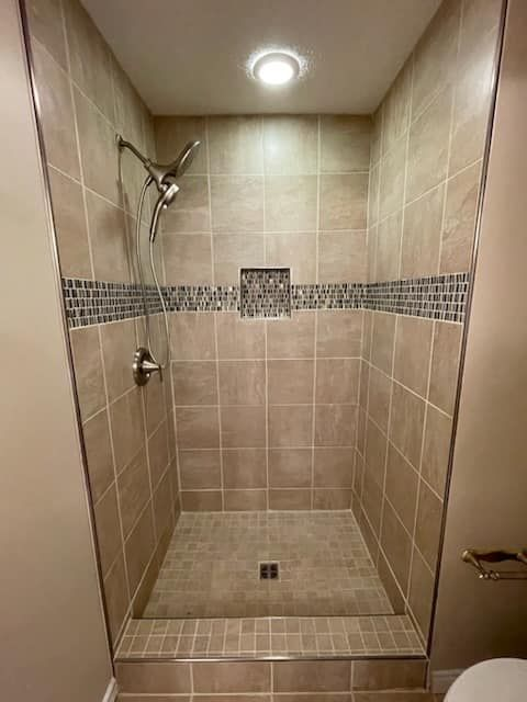 Tiled walk-in shower with tan tiles and a mosaic accent. Showerhead and recessed light fixtures.