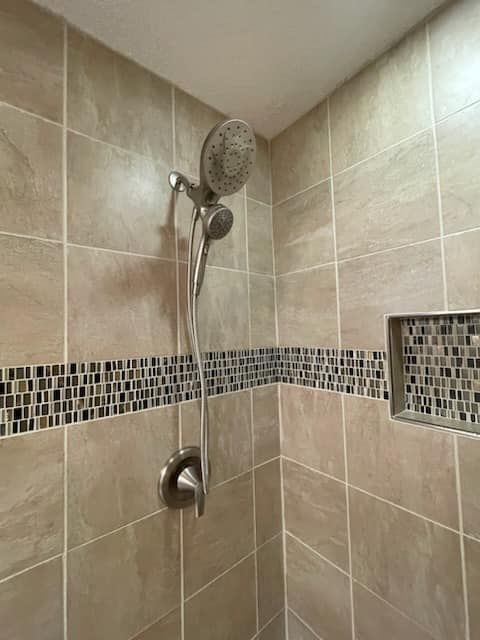 Shower with beige tile, mosaic accent, and handheld showerhead.