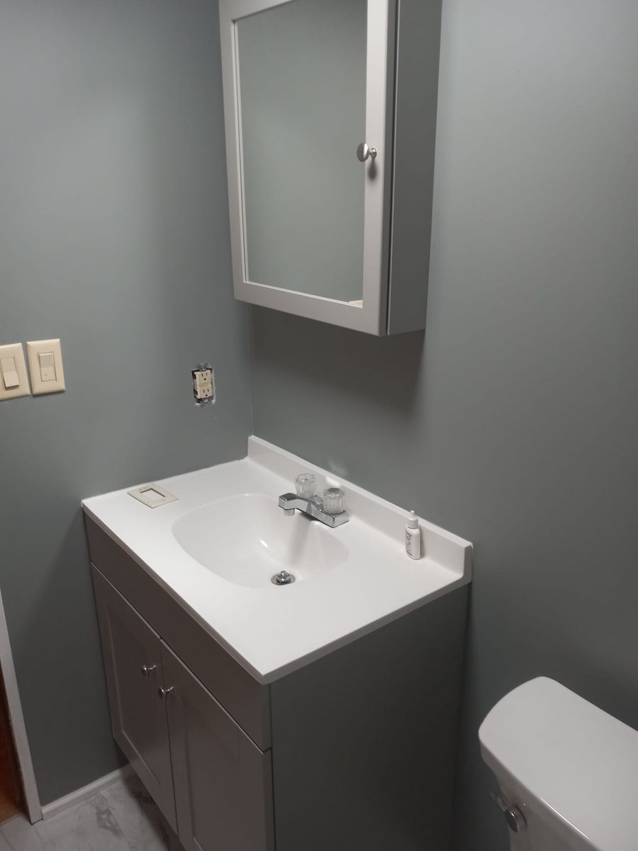Bathroom with gray walls, white sink, cabinet, mirror, and toilet.