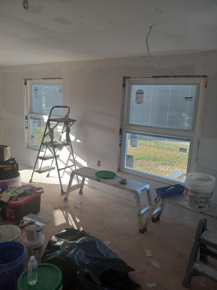 Room under renovation with two windows, ladder, and construction materials.