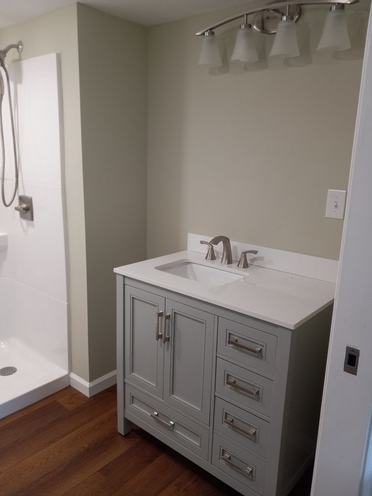 Bathroom with gray vanity, white countertop, and shower stall; dark wood floor, pale green walls.