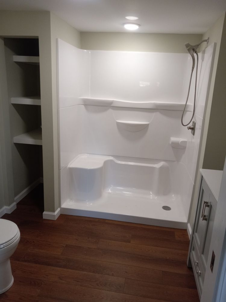 Bathroom with white shower stall, toilet, cabinetry, and dark wood floor.