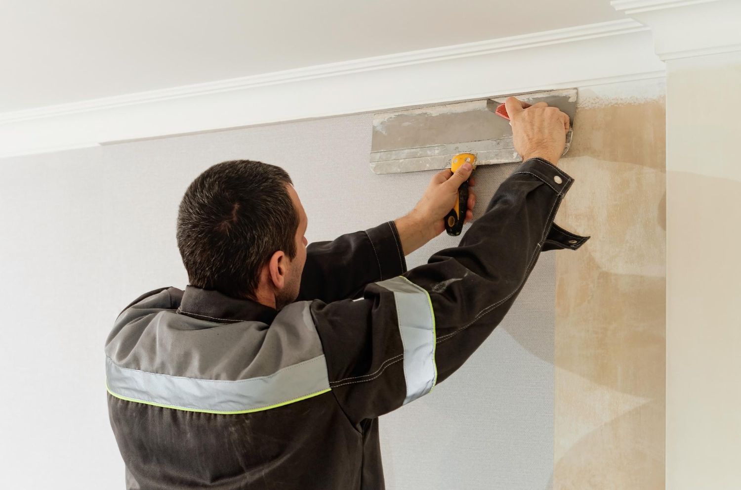 Man in work clothes using a trowel to apply plaster to a wall, near a molding.