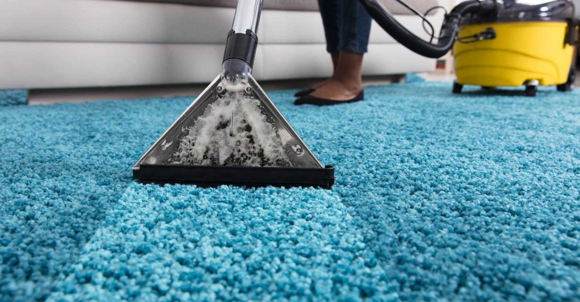 Person cleaning a turquoise rug with a yellow carpet cleaner.