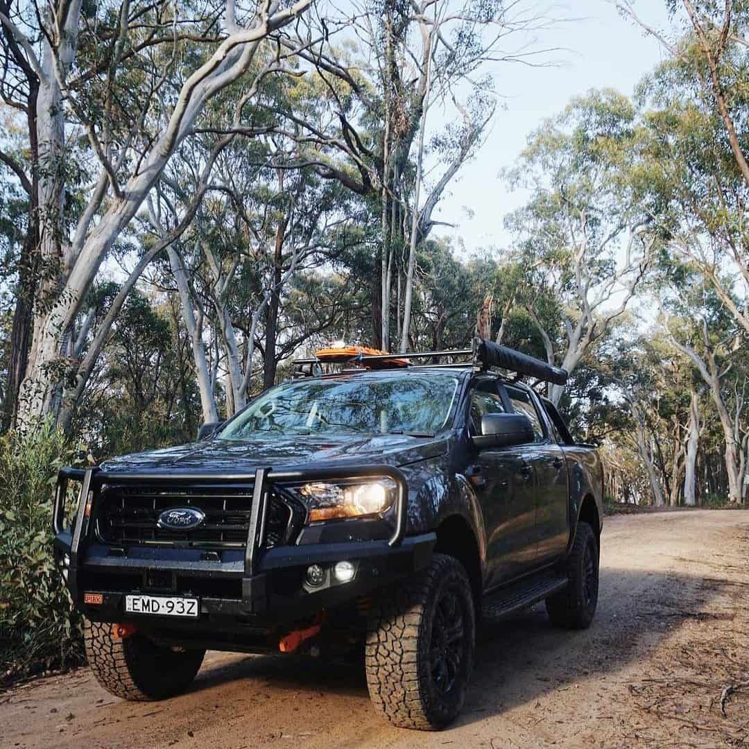 A Black Truck With A Surfboard On The Roof Is Parked On A Dirt Road — Opposite Lock In Wodonga, VIC