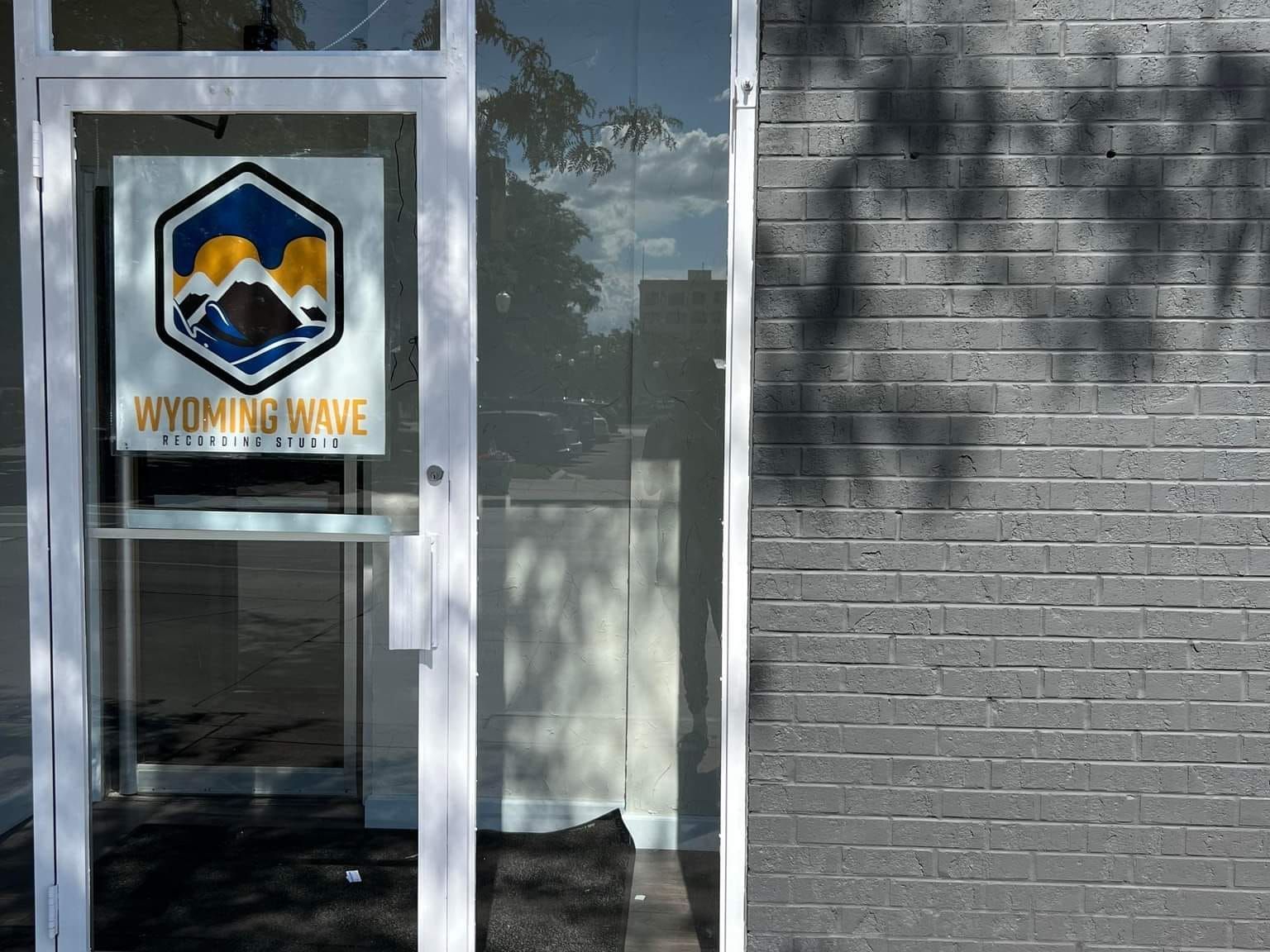 Exterior of Wyoming Wave business with a logo on the glass door. Gray brick wall on right.