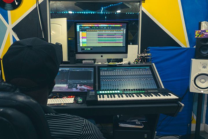 Person in recording studio, working on audio; monitors and sound mixing board visible.