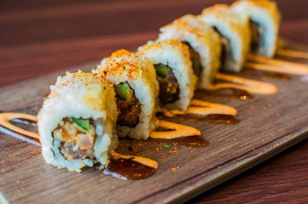 A row of sushi rolls sitting on top of a wooden cutting board.