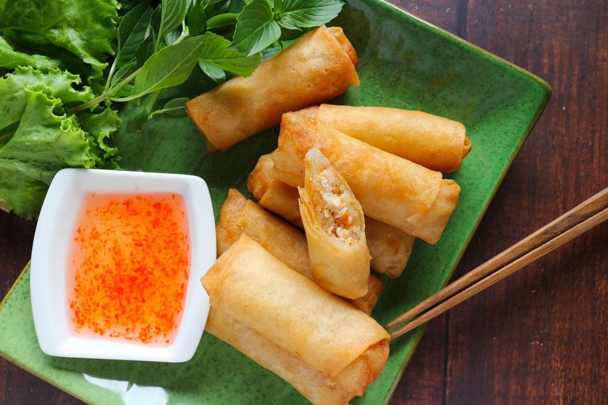 A green plate topped with spring rolls and a bowl of dipping sauce.