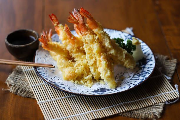 A plate of shrimp tempura with chopsticks on a bamboo mat on a wooden table.