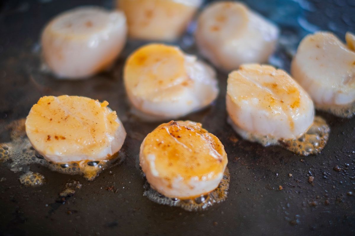Scallops are being cooked in a frying pan.