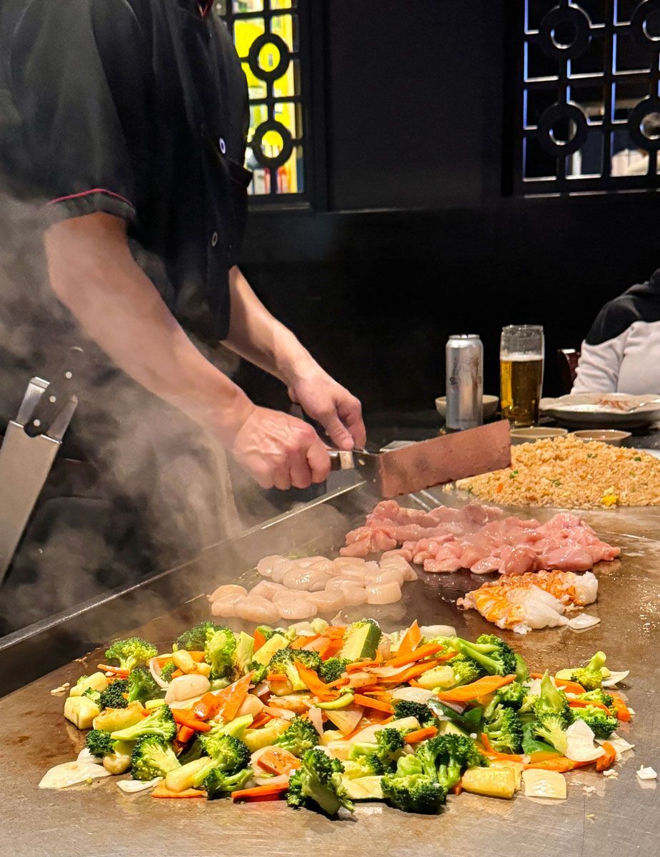 A man is cooking vegetables on a grill in a restaurant.