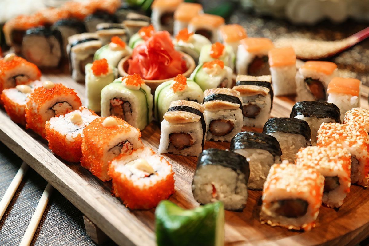 A wooden cutting board topped with a variety of sushi rolls and chopsticks.