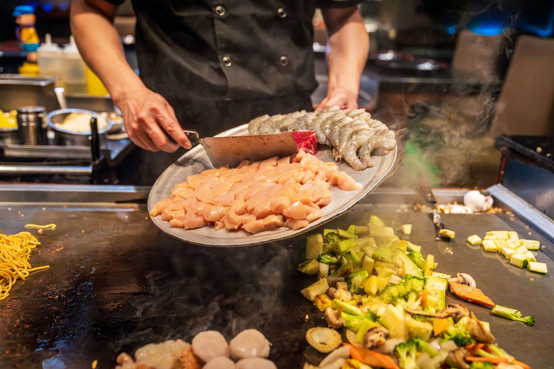 Chef grilling shrimp, chicken, and vegetables on teppanyaki grill. Chef grilling shrimp, chicken, and vegetables on teppanyaki grill.