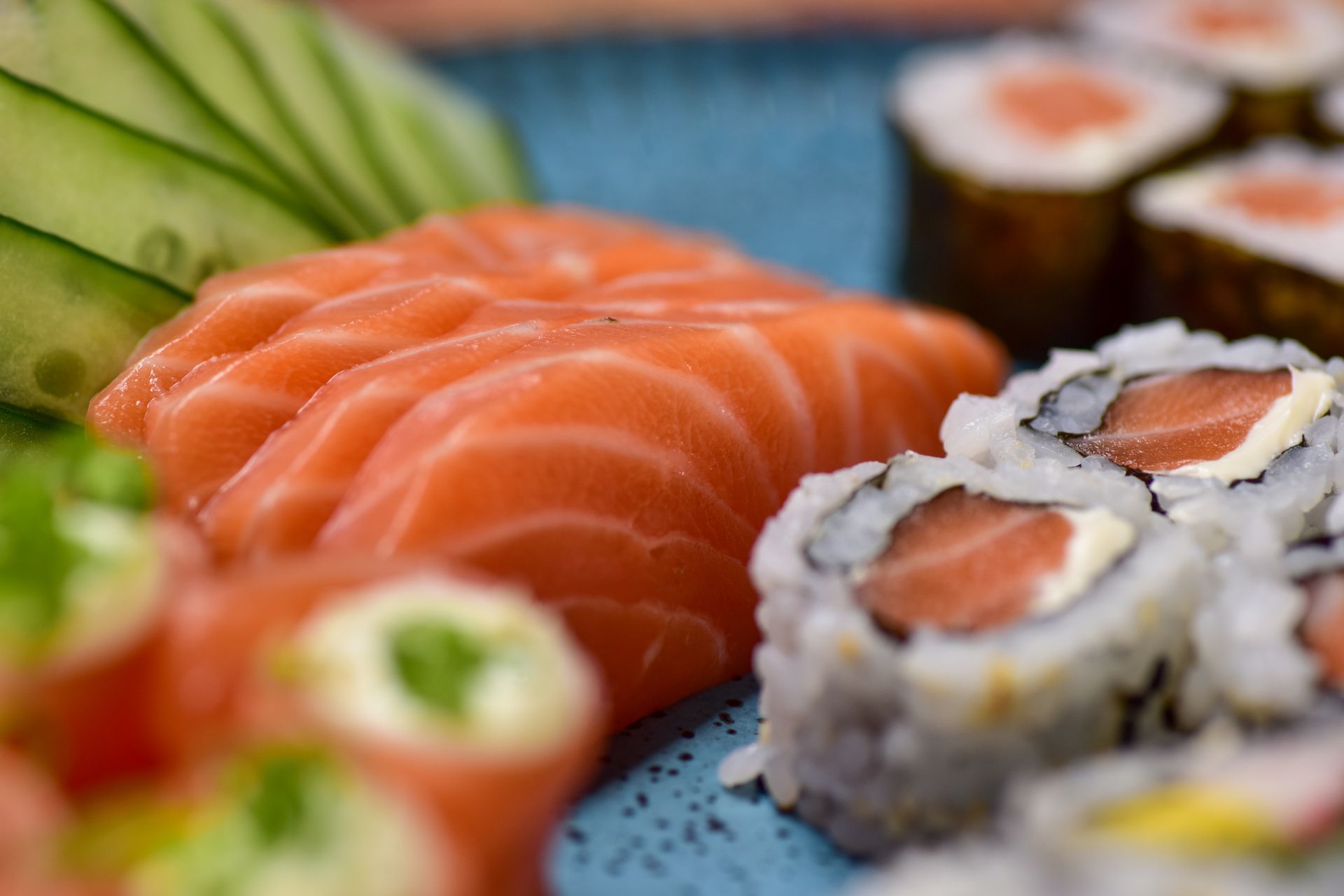 Assorted sushi rolls and salmon sashimi served with cucumber slices on a plate.