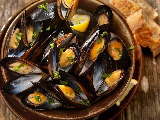 A bowl of mussels with lemon and parsley on a wooden table.