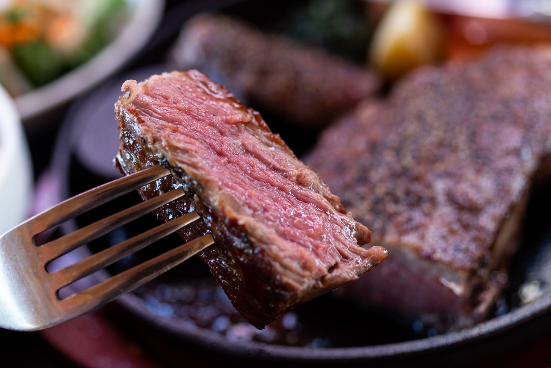 Close-up of a tasty steak piece being held up by a fork.