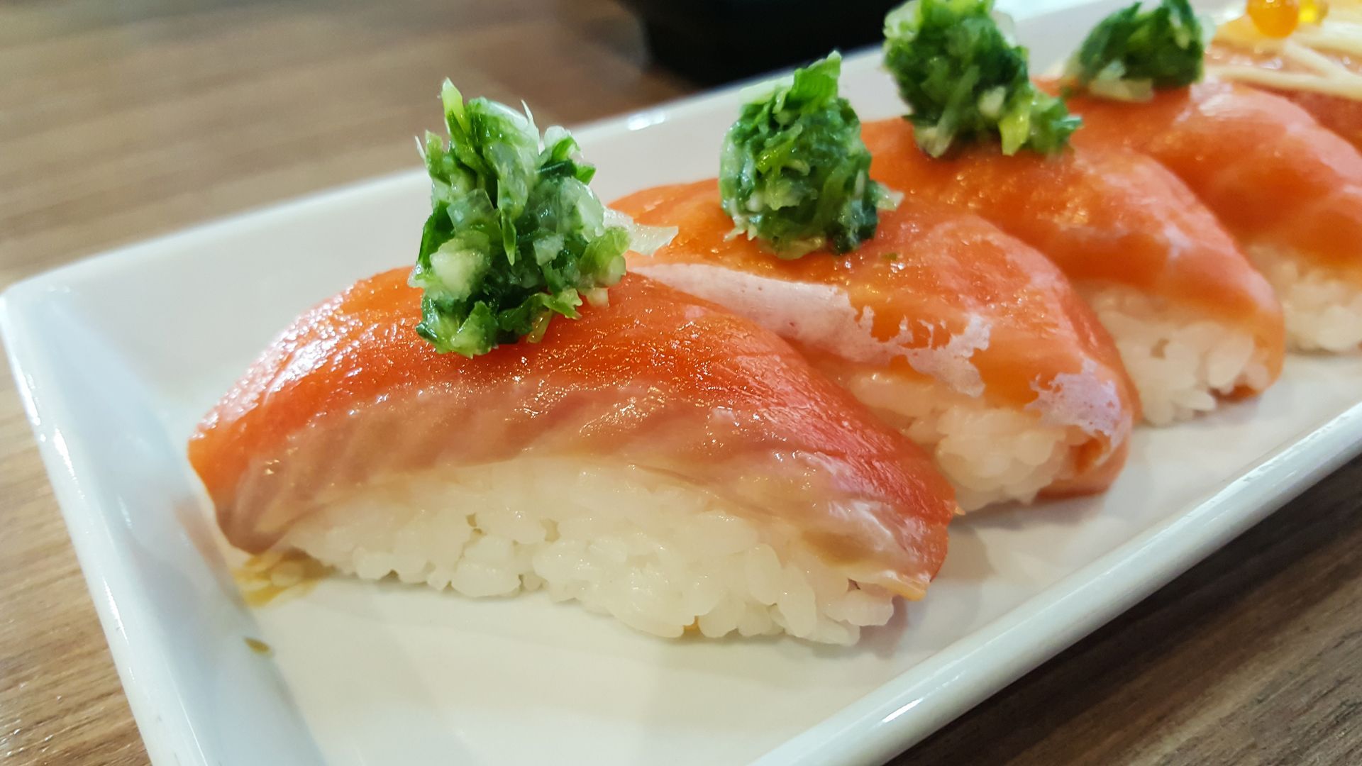 Close-up of sushi salmon adorned with wasabi on a white plate.