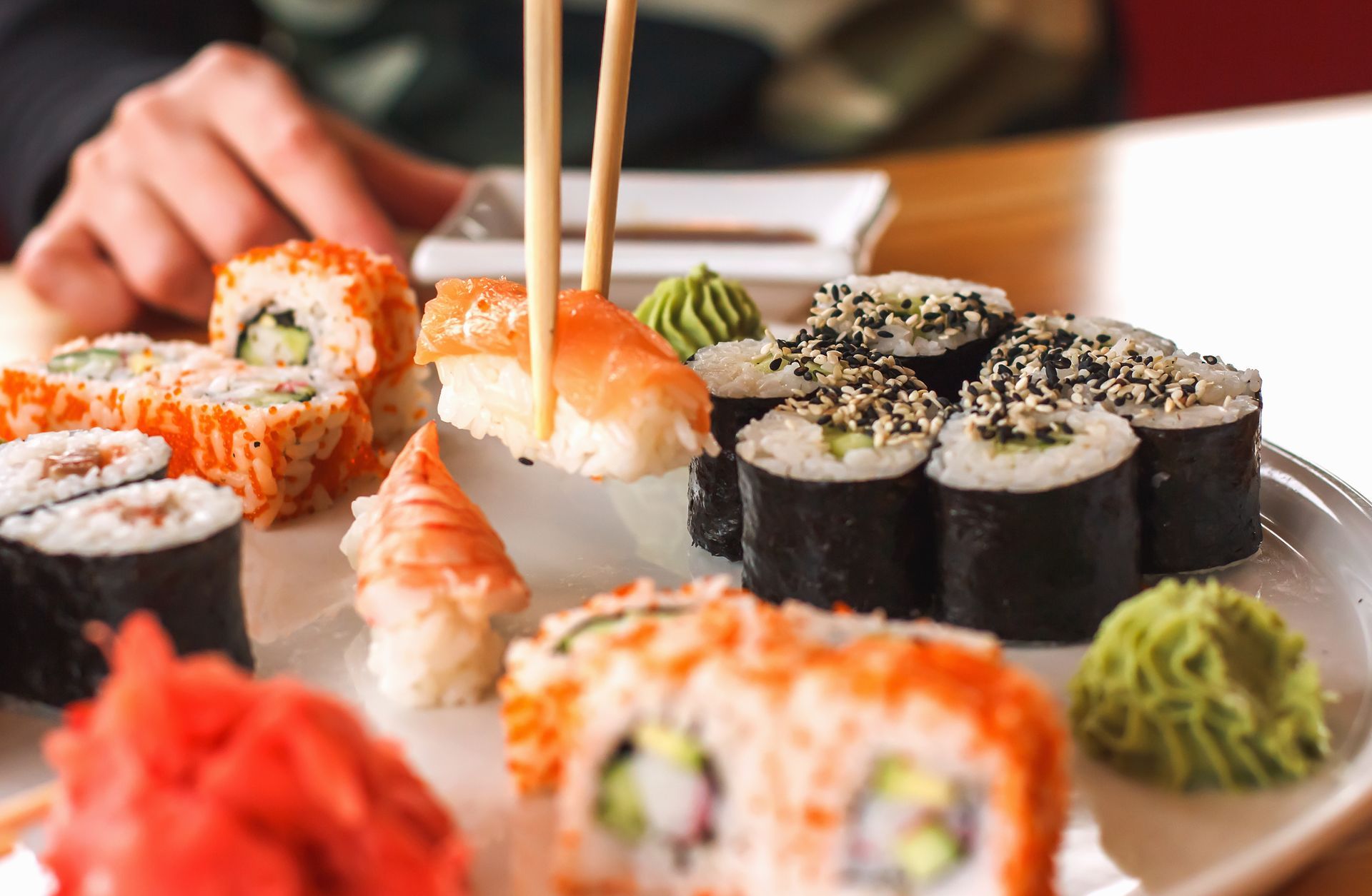 Close-up of a person grabbing sushi off an assorted plate of Japanese cuisine in a restaurant.