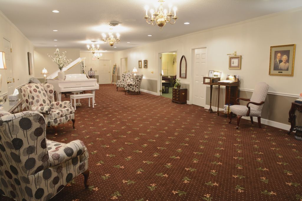 A living room with a piano , chairs , and a chandelier.