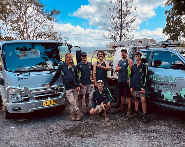 A Group Of Six Workers standing In Front Of A Ute And Truck — Puzzles Plumbing & Excavations In Koonorigan, NSW