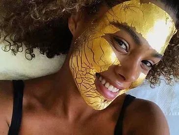 A woman is wearing a gold mask on her face and smiling