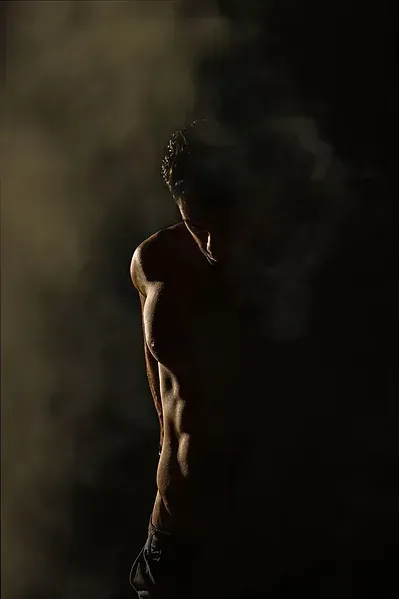 A man without a shirt is standing in the dark