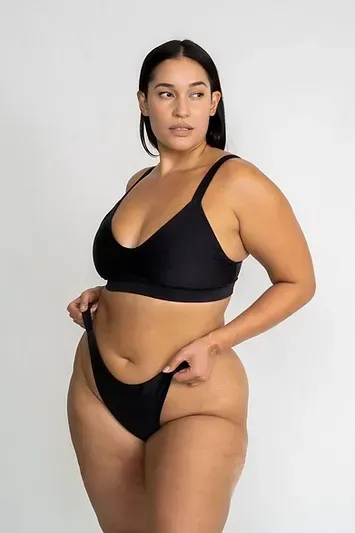 A plus size model is wearing a black bikini top and bottom