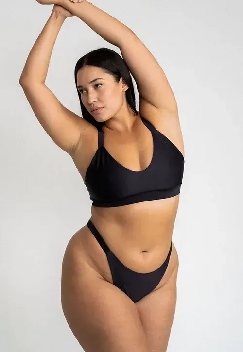 A plus size model is wearing a black bikini top and bottom