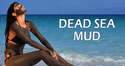 A woman is sitting on the beach with a mud mask on her face