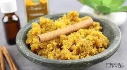 A bowl of sugar scrub with cinnamon sticks and a bottle of essential oil
