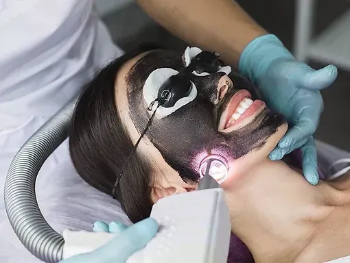 A woman is getting a charcoal mask on her face